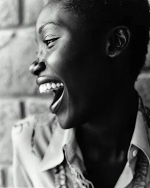 Portrait of a smiling woman in a white shirt leaning against a sunlit wall